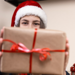 Girl in santa claus hat talks and gives a gift using laptop